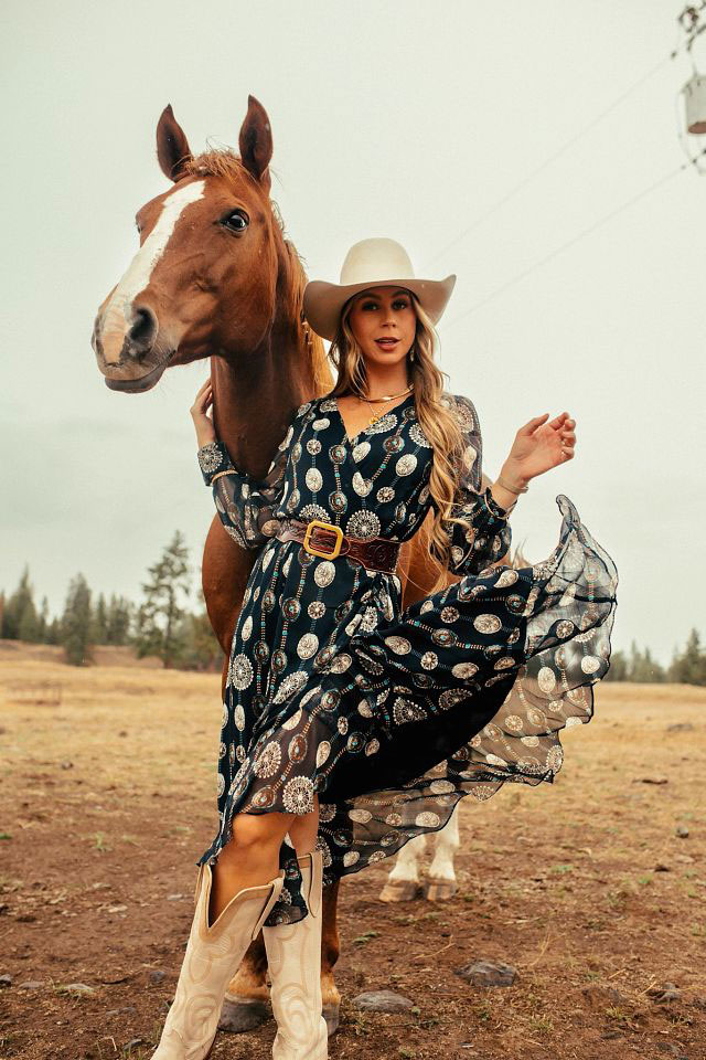 A woman wearing Justin boots standing in front of a horse.